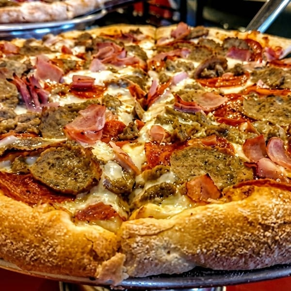 Close-up of a meat lover's pizza with pepperoni, sausage, and ham on a metal tray.