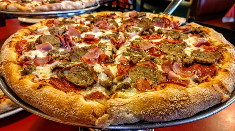Close-up of a meat lover's pizza with pepperoni, sausage, and ham on a metal tray.