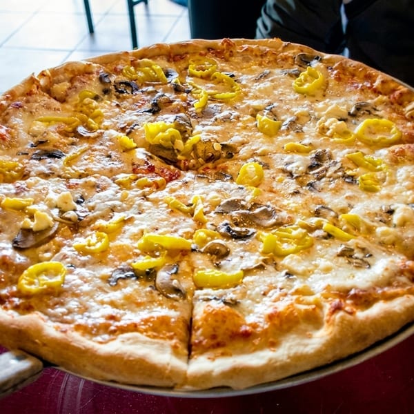 Large pizza with melted cheese, mushrooms, and yellow peppers, served on a metal tray.