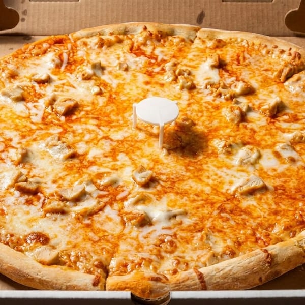 A whole chicken pizza with melted cheese and a pizza saver in a cardboard box.