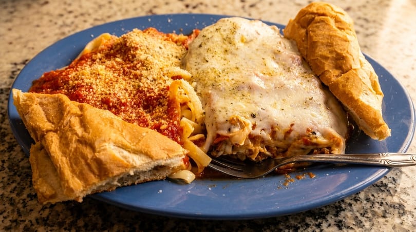 A blue plate with lasagna, spaghetti with red sauce and parmesan, and two pieces of bread.